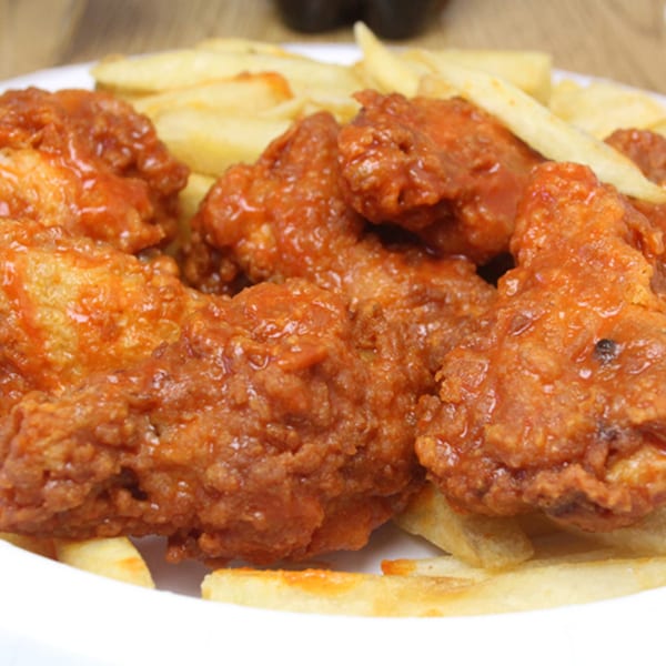 Backwoods Pizza's crispy, saucy chicken wings and golden french fries on a white plate.