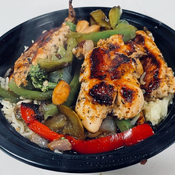 Grilled chicken with bell peppers, broccoli, and onions over rice in a black bowl.