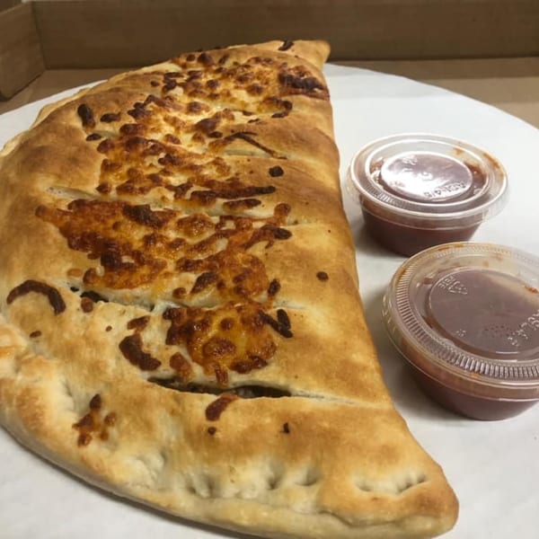 A golden-brown calzone with melted cheese on top, served with two small containers of marinara sauce.