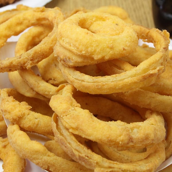 A close-up of golden-brown, crispy onion rings from Backwoods Pizza, piled high in a white container.