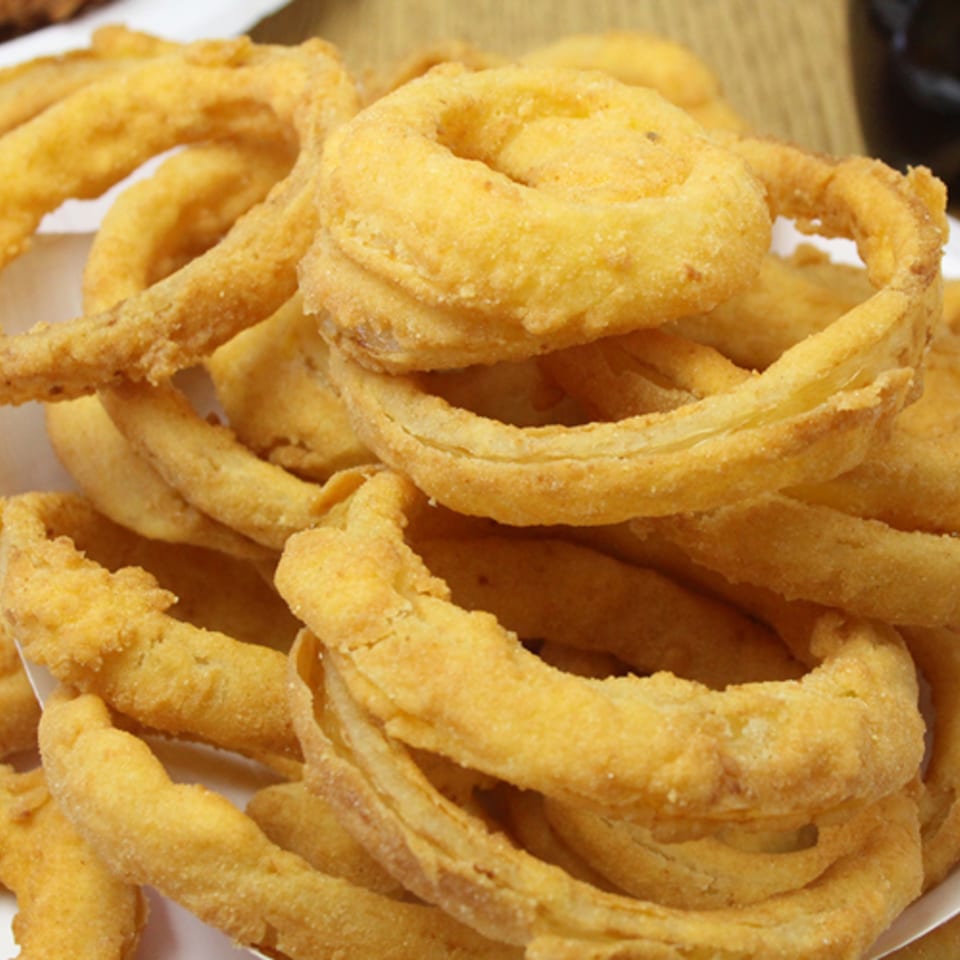 A close-up of golden-brown, crispy onion rings from Backwoods Pizza, piled high in a white container.