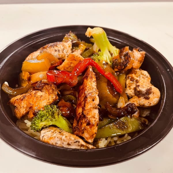 A close-up of a chicken and vegetable stir-fry with broccoli, peppers, and onions over rice in a black bowl.
