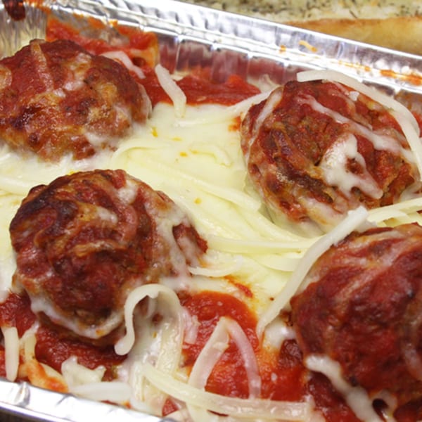 Four large meatballs covered in red sauce and melted white cheese in a foil container.