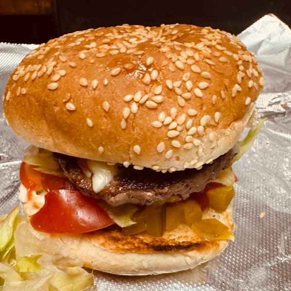 A Backwoods Pizza burger with sesame seed bun, patty, lettuce, tomato, pickles, and sauce.